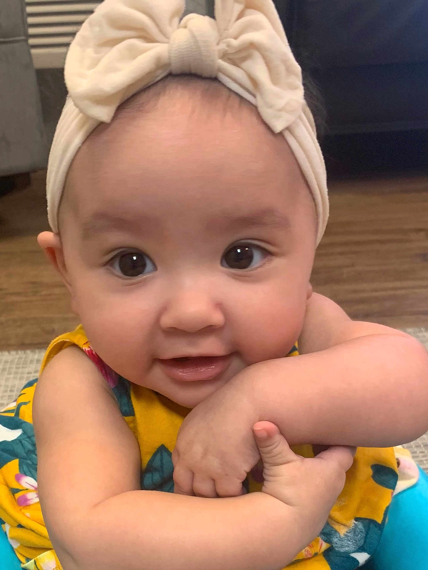 Grace joined the competition — help win amazing prizes! baby, infant, child, headband, bow, smile, face, arm, hand, yellow_clothing, floral_pattern, indoors, floor, wooden_floor, cute, closeup, happy, person, skin, portrait