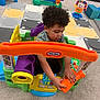 child, toddler, curly_hair, toy, playroom, carpet, puzzle_mat, activity_center, colorful, indoor, plastic_toy, hands, floor, furniture, baby_toys, engaged, cute, early_childhood, learning, fun