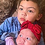 child, baby, couch, pillow, curly_hair, red_bow, mittens, blue_clothing, soft_toys, indoor, portrait, cute, siblings, family, toddler, infant, closeup, candid, warm, cozy