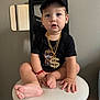 baby, toddler, child, face, cap, baseball_cap, gold_chain, dollar_pendant, stool, chair, indoor, portrait, black_tshirt, barefoot, bracelet, mirror, wall, hands, legs, cute