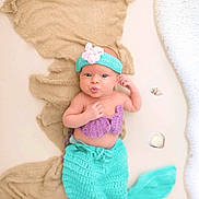 Raelynn is registered to the contest to win money with this photo: baby, mermaid, costume, headband, flower, seashells, fabric, foam, puckered_lips, lying_down, purple, turquoise, cute, infant, portrait, hand_near_face, soft_texture, playful, ocean_theme, decorative