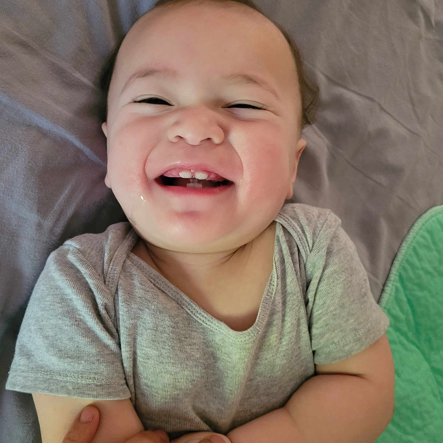 Zachary is registered to the contest to win money with this photo: baby, smile, happy, infant, face, hands, clothing, lying_down, skin, person, cute, joy, child, toddler, bed, fabric, adult_hand, casual_wear, closeup, cheerful