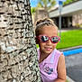 Zyli joined the competition — help win amazing prizes! child, tree, pink_sunglasses, smile, outdoor, daylight, cartoon_patch, purple_shirt, playful, young_girl, hand_on_tree, short_hair, casual_clothing, side_pose, green_grass, blurred_background, building, sidewalk, reflection, nature