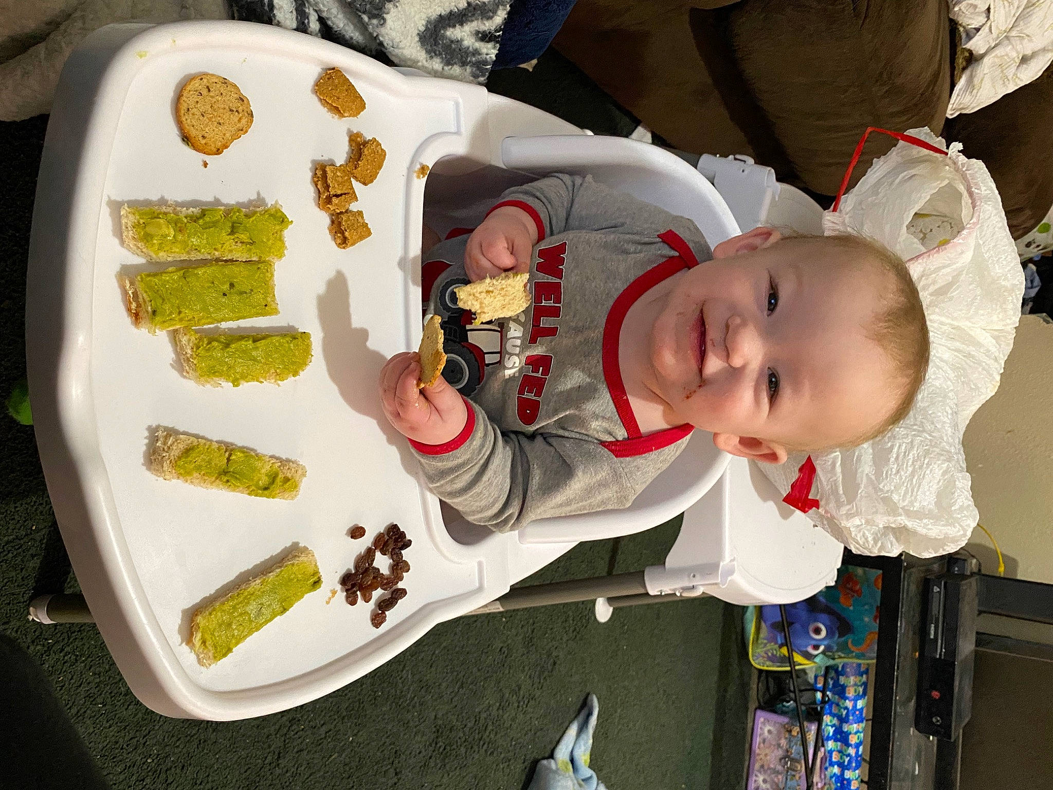 Elliott is registered to the contest to win money with this photo: baby, baby_products, baby_toddler_clothing, child, comfort_food, culinary_art, dishware, finger_food, food, fun, hat, joy, pattern, person, plate, room, sitting, sleeve, tableware, toddler