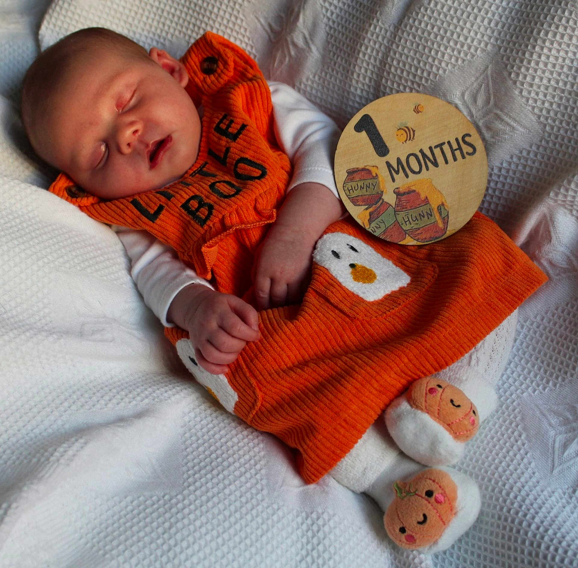 Oliwia joined the competition — help win amazing prizes! baby, sleeping, orange_clothing, white_blanket, milestone_sign, plush_slippers, infant, cute, cozy, hand, face, newborn, soft_texture, smile, wooden_sign, baby_outfit, resting, child, portrait, indoors
