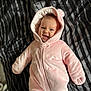 baby, infant, pink_onesie, hood, smile, happy, lying_down, striped_blanket, soft_texture, cute, child, face, warm_clothing, indoors, cozy, newborn, adorable, person, portrait, expression
