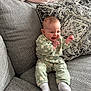 baby, infant, smiling, happy, couch, sofa, pillow, blanket, green_clothing, socks, indoor, face, person, home, cute, seated, patterned_pillow, cozy, expression, child