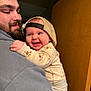 baby, child, man, cap, backward_cap, beard, smile, happy, hug, indoor, cozy, hoodie, clothing, face, person, expression, warmth, affection, portrait, casual