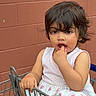 Aleezay joined the competition — help win amazing prizes! toddler, child, shopping_cart, brick_wall, outdoor, curly_hair, white_dress, floral_pattern, fingers_in_mouth, casual, daylight, person, cute, expression, sitting, playful, young_child, candid, urban, footwear