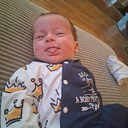 Bryson is registered to the contest to win money with this photo: baby, infant, tongue_out, crown_pattern, onesie, cushion, striped, wood_floor, indoor, cute, face, smiling, child, person, home, casual, playful, relaxed, sitting, clothing