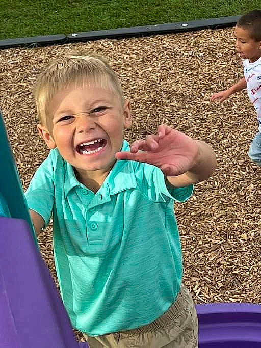 David is registered to the contest to win money with this photo: blue, child, face, finger, fun, gesture, grass, green, happy, head, human, leaf, leisure, mouth, person, public_space, skin, sleeve, smile, thumb