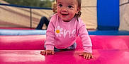 Alayna is registered to the contest to win money with this photo: toddler, child, smiling, pink_sweater, bow, curly_hair, crawling, bounce_house, inflatable, playground, outdoor, happy, cute, person, young_child, colorful, fun, daylight, portrait, play