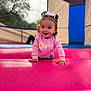 toddler, child, smiling, pink_sweater, bow, curly_hair, crawling, bounce_house, inflatable, playground, outdoor, happy, cute, person, young_child, colorful, fun, daylight, portrait, play