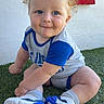 Jesse is registered to the contest to win money with this photo: baby, blue_eyes, casual, child, curly_hair, cute, drool, grass, happy, outdoor, playful, portrait, red_sign, sign, sitting, smile, sneakers, sporty_clothing, wall, young_child