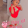 child, girl, posing, red_shirt, beige_skirt, hair_bows, indoor, carpet, refrigerator, home, smiling, cute, school, celebration, text_overlay, heart_emoji, floor, wall, person, young