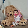 baby, child, teddy_bear, plush_toy, pacifier, pajamas, carpet, indoor, smiling, cute, toy, sitting, happy, infant, playtime, childhood, soft_toy, cozy, home, adorable