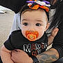 Athena joined the competition — help win amazing prizes! baby, pacifier, headband, tattoo, arm, black_shirt, indoor, carpet, person, child, holding, cute, eyes, face, hand, adult, clothing, halloween, black_hair, sitting