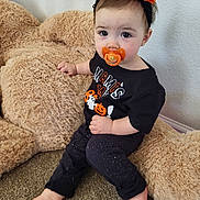 Athena joined the competition — help win amazing prizes! toddler, child, pacifier, headband, halloween, black_clothing, teddy_bear, plush_toy, carpet, indoor, cute, baby, sitting, barefoot, expression, wall, decorative, orange, black, holiday