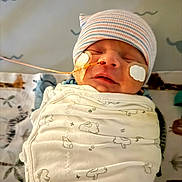Noah is registered to the contest to win money with this photo: baby, bed, blanket, close_up, electrodes, family, fragile, healthcare, hospital, indoors, infant, medical_monitor, monitoring_leads, newborn, peaceful, portrait, resting, sleeping, striped_hat, swaddled