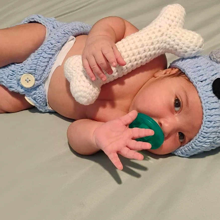 Liam is registered to the contest to win money with this photo: baby, infant, child, lying_down, bed, indoors, crocheted_clothing, elephant_costume, blue_hat, stuffed_toy, knitted_toy, pacifier, white_diaper, bare_feet, portrait, close_up, smiling, playful, textile, home