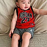 Ali is registered to the contest to win money with this photo: baby, child, infant, couch, clothing, red_jersey, gray_shorts, barefoot, indoor, person, sitting, cute, relaxed, looking_sideways, soft_fabric, cushion, home, portrait, young_child, comfortable