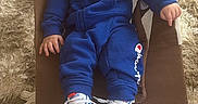 Ali joined the competition — help win amazing prizes! baby, child, blue_clothing, tracksuit, sneakers, baby_rocker, carpet, plush_toys, indoor, person, footwear, casual_wear, infant, cute, relaxed, soft_texture, floor, seated, young_child, cozy