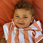 Paul participe au concours pour gagner de l'argent avec cette photo : toddler, child, smiling, curly_hair, towel, orange, white, striped, portrait, close_up, happy, cute, baby, face, skin, eyes, person, indoors, cozy, background