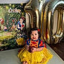 Ashley joined the competition — help win amazing prizes! apple, backdrop, balloons, birthday, blue_top, celebration, child, costume, curly_hair, disney, dress, floor_mat, indoor, number_balloons, party, red_bow, smiling, snow_white, toddler, yellow_skirt