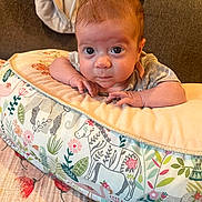 Violet is registered to the contest to win money with this photo: baby, infant, newborn, decorative_pillow, cushion, couch, blanket, floral_pattern, animal_illustration, wide_eyes, gaze, portrait, hands, skin, cozy, indoor, fabric, head, resting, adorable