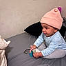 baby, child, pink_hat, pajamas, bed, blanket, black_pillow, pacifier, indoor, cute, infant, sitting, focus, soft_lighting, young_child, knit_hat, cozy, person, sleepwear, toy