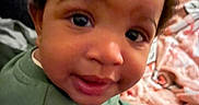 Bryson is registered to the contest to win money with this photo: baby, blanket, child, closeup, cozy, curly_hair, cute, eyes, face, green_clothing, happy, indoors, infant, person, playtime, portrait, sitting, smile, toy, young_child
