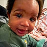 Bryson is registered to the contest to win money with this photo: baby, child, face, eyes, smile, green_clothing, indoors, blanket, toy, curly_hair, cute, infant, sitting, closeup, portrait, person, young_child, happy, cozy, playtime