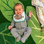 Rhys is registered to the contest to win money with this photo: baby, smiling, infant, carpet, green, leaf_pattern, bib, game_face, onesie, sports_theme, happy, cute, lying_down, clothing, footed_pajamas, child, indoors, playful, toddler, face