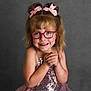 background, child, cute, expressive, fashion, girl, glasses, hair_buns, hands_clasped, happy, innocent, joy, pink_bows, pink_dress, portrait, sequin, smile, sparkly, studio, young