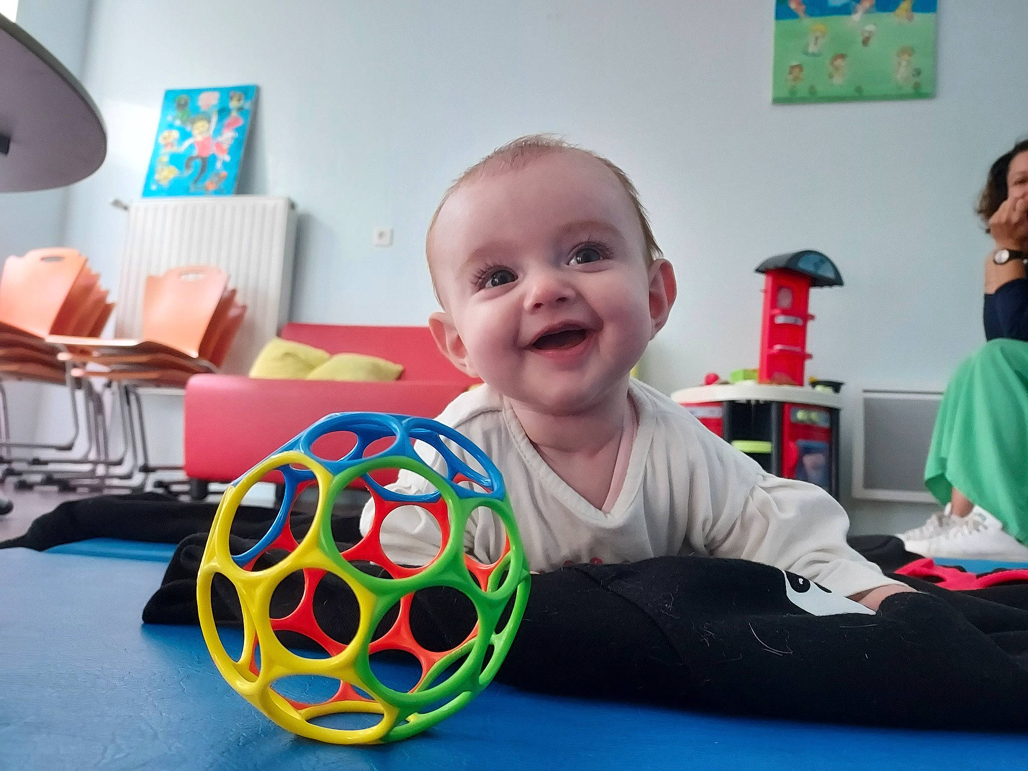 Hilda a rejoint le concours — aidez-le/la à gagner de superbes lots ! art, baby, baby_playing_with_toys, baby_products, baby_toys, ball, child, flooring, fun, green, joy, leisure, pattern, person, play, room, sitting, smile, soccer_ball, t_shirt