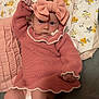 baby, infant, pink_dress, headband, bow, pillow, floral_pattern, blanket, diaper, socks, cute, indoors, child, person, portrait, knitwear, laying_down, soft_lighting, expression, fashion