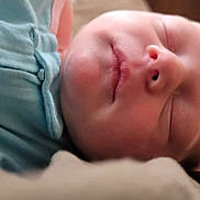 Ellie is registered to the contest to win money with this photo: baby, sleeping, close_up, face, infant, soft_lighting, cozy, blue_outfit, blanket, peaceful, skin, nose, mouth, eyelids, head, newborn, indoors, portrait, resting, child