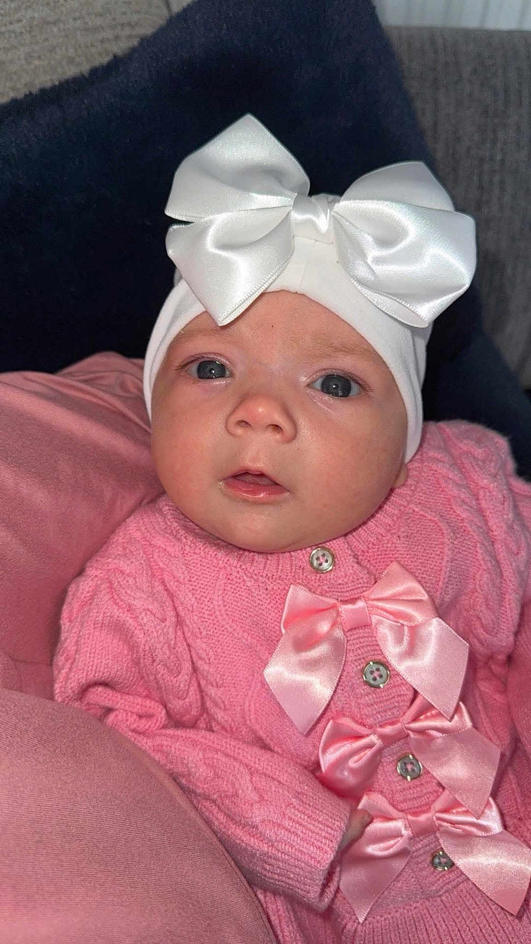 Aurora-Rose is registered to the contest to win money with this photo: adorable, baby, baby_face, blanket, bows, buttoned_sweater, child, closeup, cute, headband, indoors, infant, looking_at_camera, newborn, pink_sweater, portrait, small_hands, soft_texture, warm_clothing, white_bow