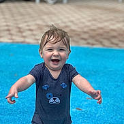 Owen is registered to the contest to win money with this photo: baby, blue_surface, candid, child, daylight, face, happy, joyful, legs, onesie, outdoor, playground, pool_area, portrait, smiling, splash_pad, summer, toddler, water_play, wet_hair