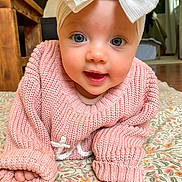 Sutton joined the competition — help win amazing prizes! baby, child, headband, bow, blue_eyes, pink_sweater, knitwear, crawling, blanket, floral_pattern, indoor, wooden_furniture, floor, portrait, cute, smiling, face, hands, cozy, natural_light