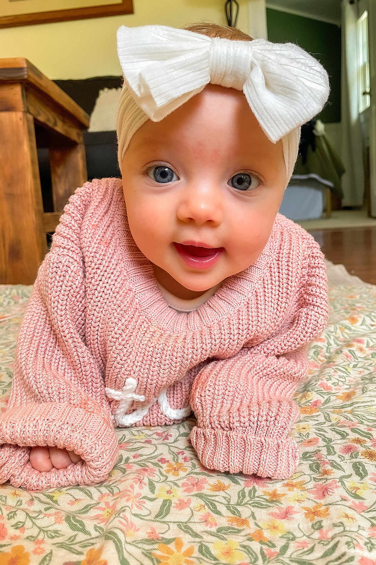 Sutton joined the competition — help win amazing prizes! baby, child, headband, bow, blue_eyes, pink_sweater, knitwear, crawling, blanket, floral_pattern, indoor, wooden_furniture, floor, portrait, cute, smiling, face, hands, cozy, natural_light
