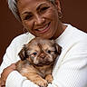 animal, brown_background, close_up, cute, dog, earrings, gray_hair, happy, holding, hugging, indoors, person, pet, photography, portrait, puppy, short_hair, smiling, white_sweater, woman