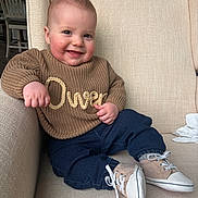 Owen is registered to the contest to win money with this photo: baby, child, smiling, sitting, indoor, armchair, clothing, sweater, pants, shoes, face, cute, happy, person, portrait, baby_shoes, furniture, cozy, head, expression