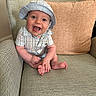 baby, child, smiling, hat, blue_clothing, plaid, armchair, cushion, happy, sitting, indoors, person, face, cute, infant, foot, hand, skin, portrait, cozy
