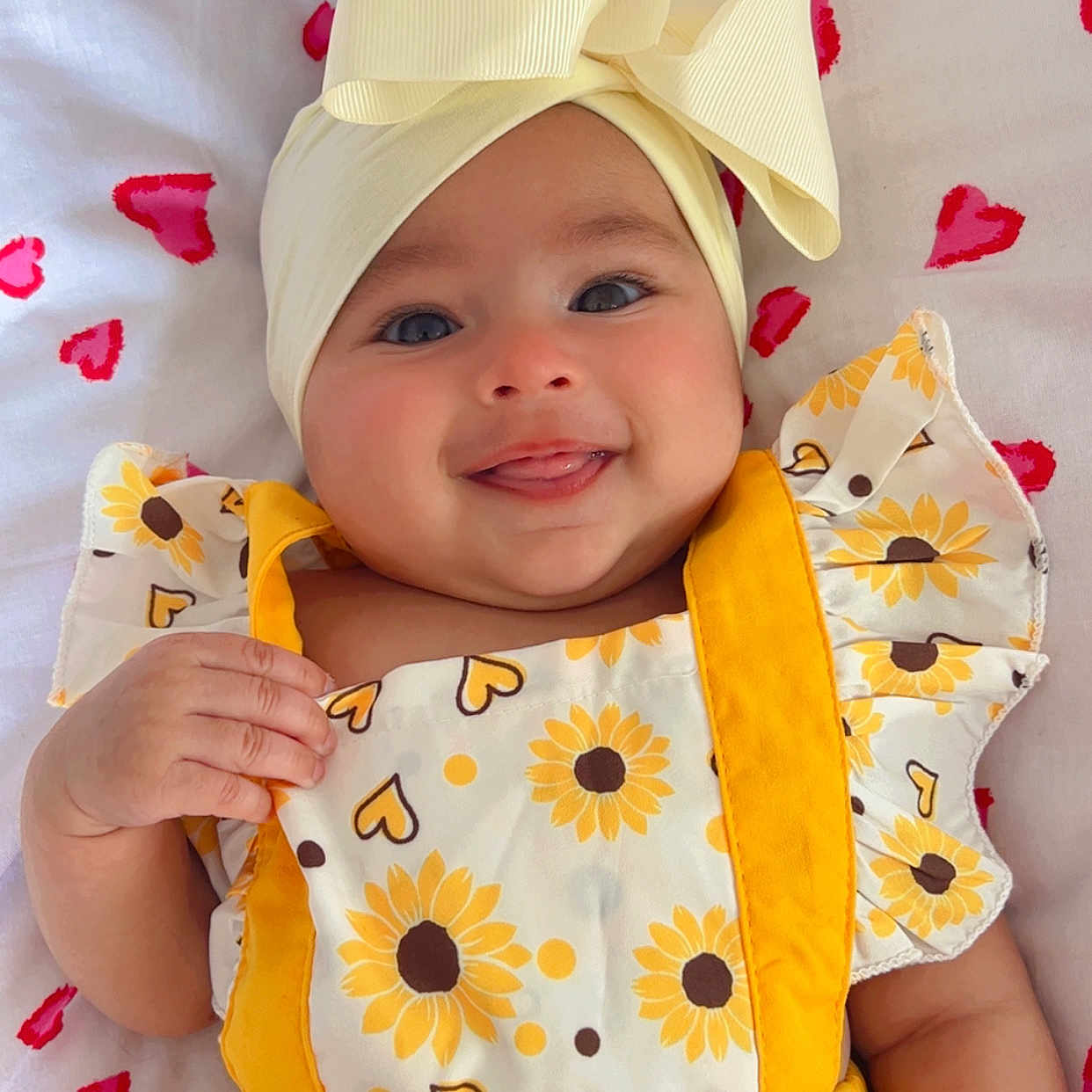 Sofia joined the competition — help win amazing prizes! baby, blanket, bow, button, child, cute, fabric, face, hand, happy, headband, hearts, infant, lying_down, playful, portrait, red_bracelet, smiling, sunflower_pattern, yellow_clothing