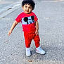 child, toddler, curly_hair, red_clothing, mickey_mouse, white_sneakers, standing, street, playful, smile, outdoor, sidewalk, casual, young, person, fashion, pose, happy, daylight, urban