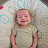 baby, smiling, infant, onesie, baby_chair, patterned_fabric, happy, child, seated, indoor, cute, young, person, face, head, skin, human, small, joyful, relaxed