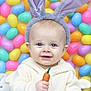 baby, bunny_ears, carrot_toy, child, colorful, cute, easter_eggs, festive, funny_hat, happy, indoors, kid, pastel_colors, playful, portrait, smiling, toy, wearing_hat, white_sweater, young_child
