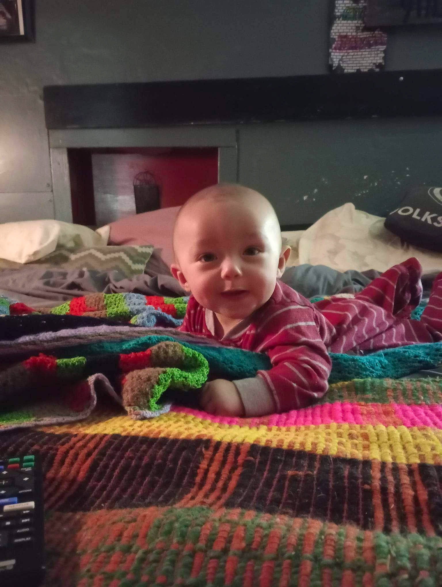 Kieran is registered to the contest to win money with this photo: baby, bedtime, carpet, child, comfort, flooring, fun, grass, linens, pattern, person, picture_frame, room, sitting, smile, t_shirt, television, textile, toddler, toy