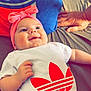 baby, smile, headband, pink, shirt, adidas, bed, pillow, hand, infant, clothing, happy, person, lying_down, bright, indoor, cute, resting, child, soft